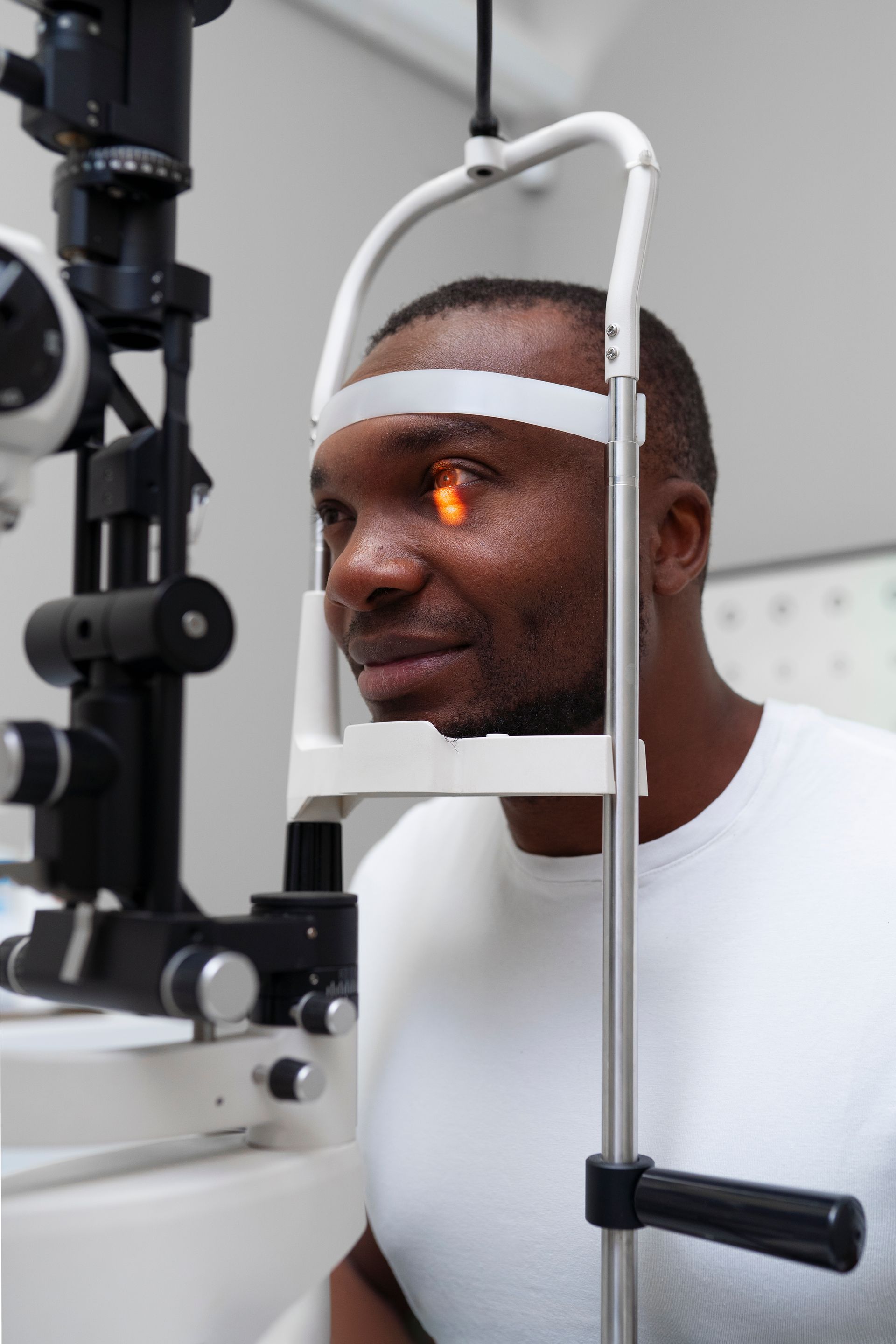 Man at an eye exam machine with orange light focused on his eye