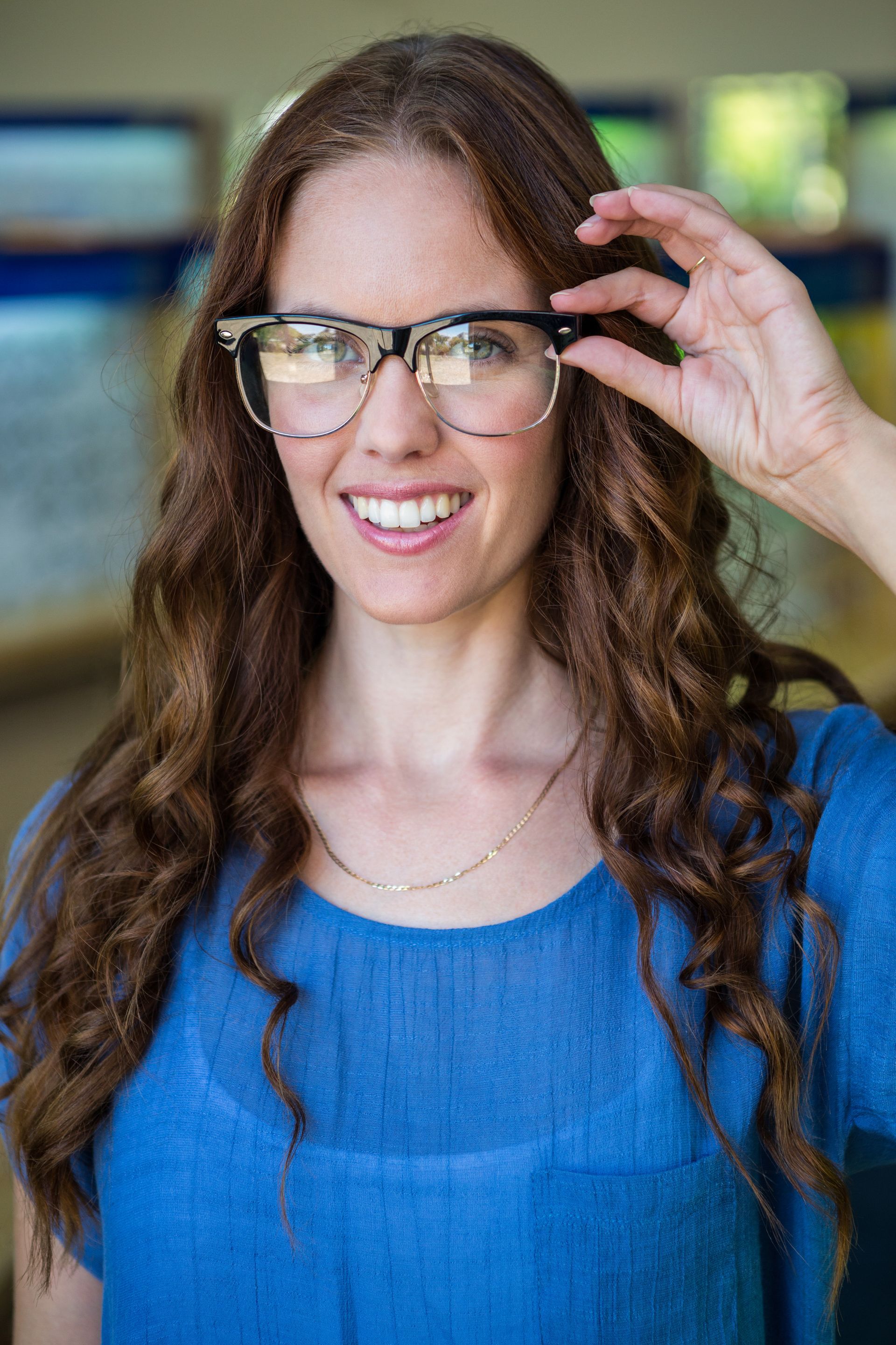 Woman in blue shirt adjusting glasses and smiling indoors