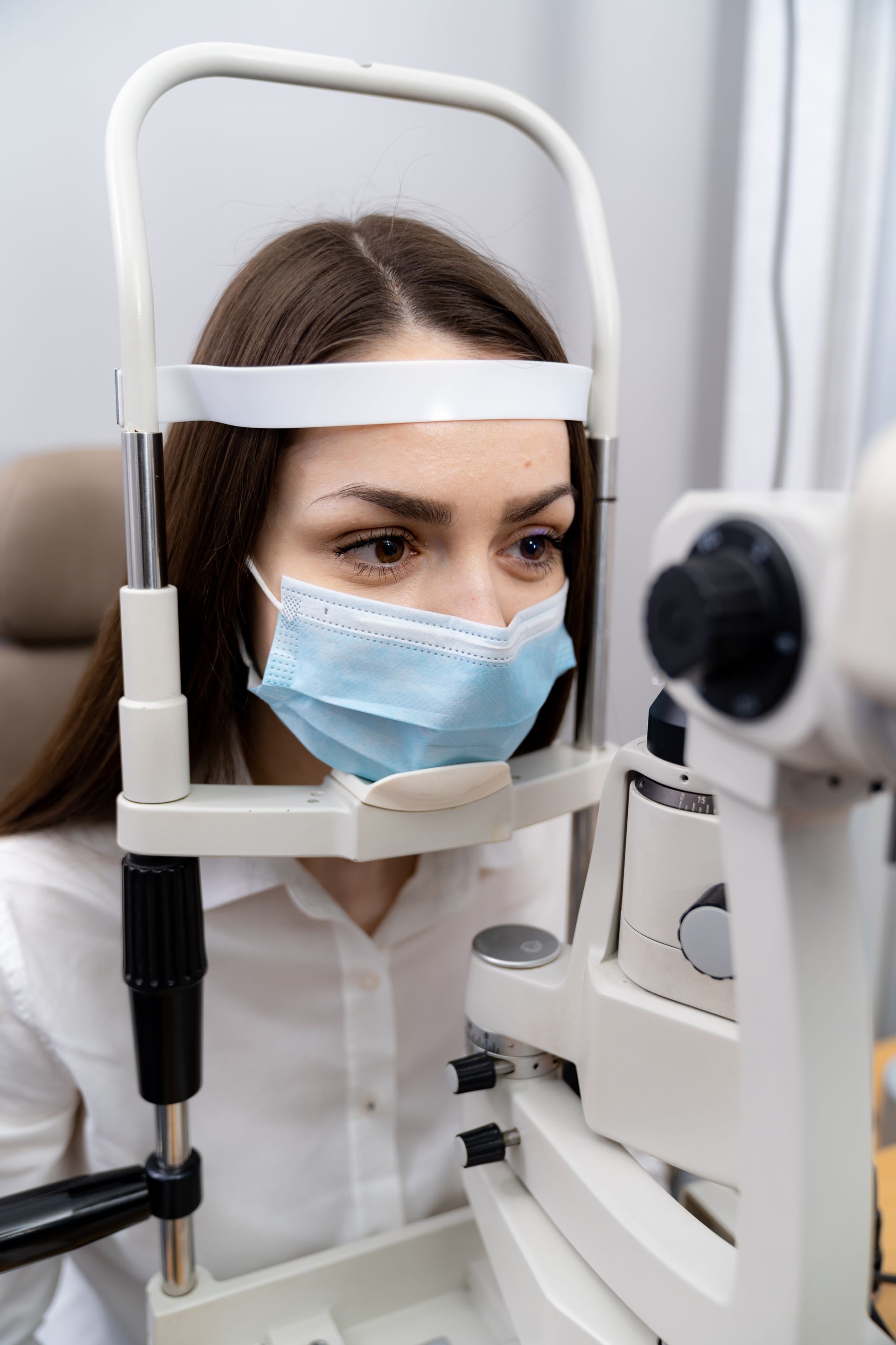 Woman wearing a blue mask looking into an eye exam machine at an optometrist office