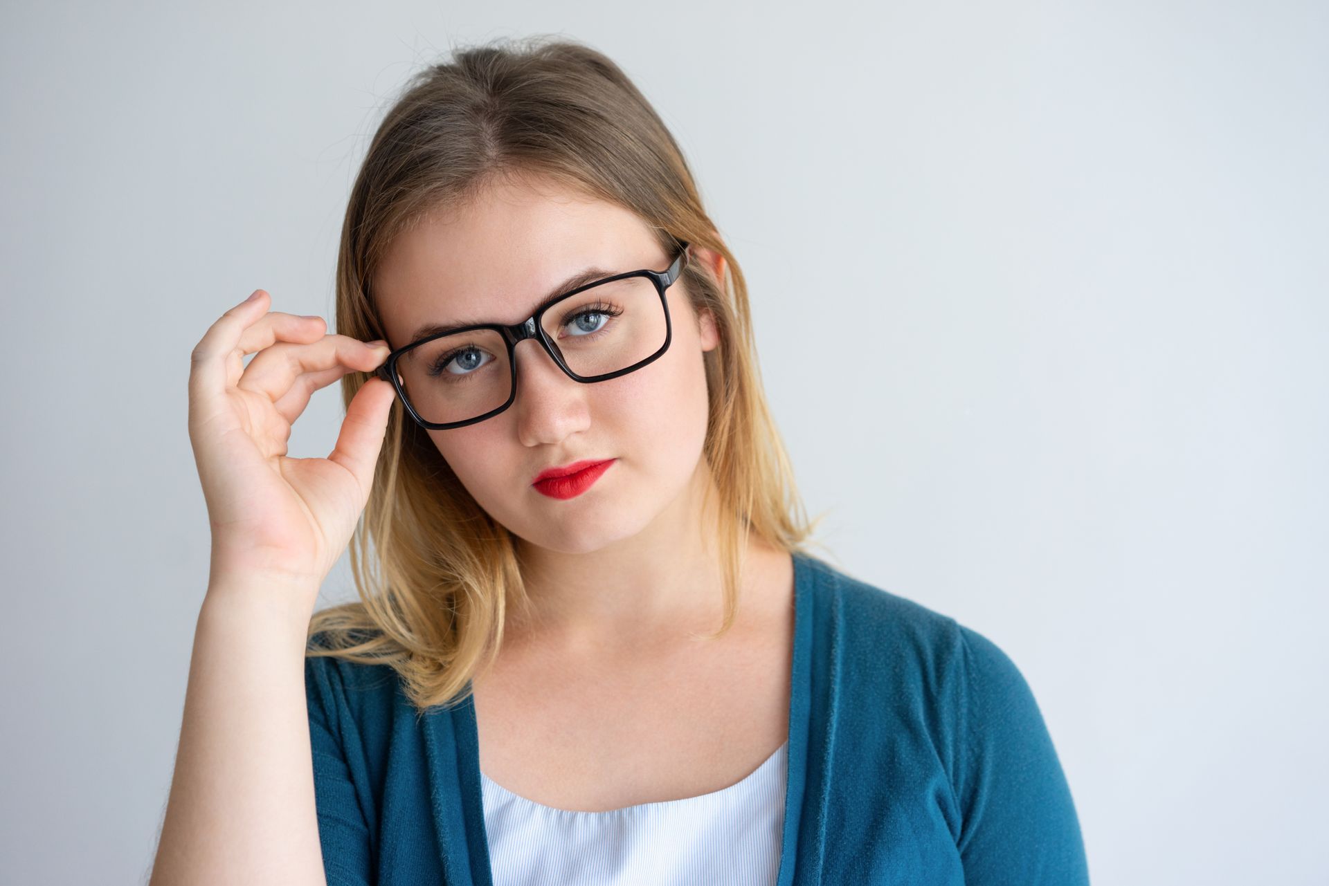 Portrait of a woman wearing glasses and a blue cardigan, adjusting them against a light background