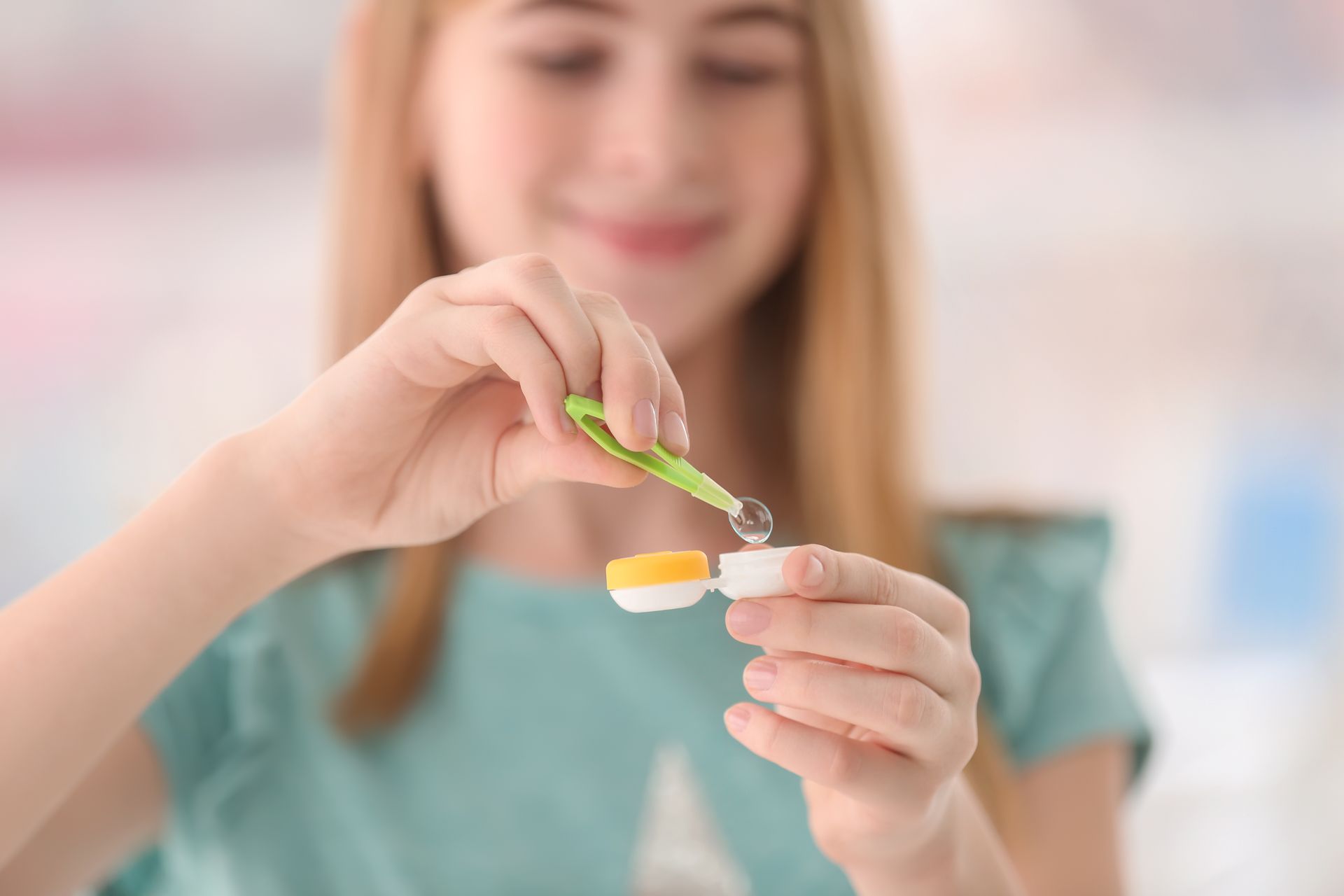 Woman holding a contact lens case and using a green tool to pick up a lens