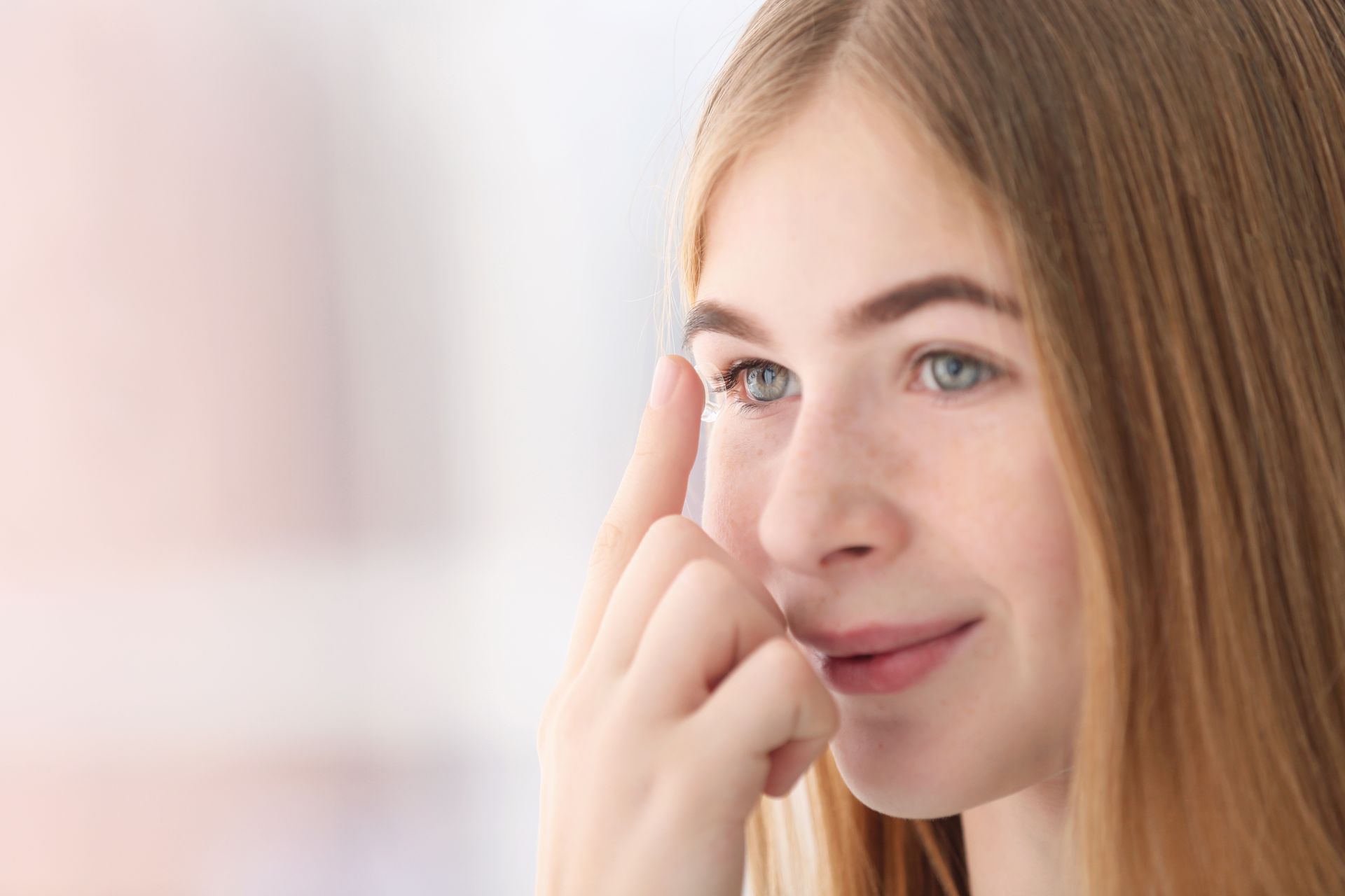 Close-up of a smiling person applying skincare cream near the eye