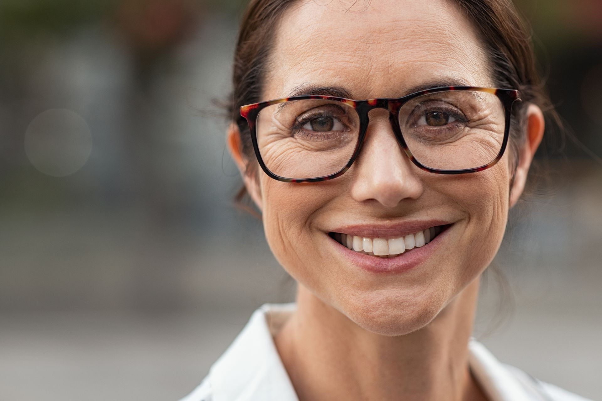 Smiling woman wearing glasses and a white shirt, with a softly blurred background.