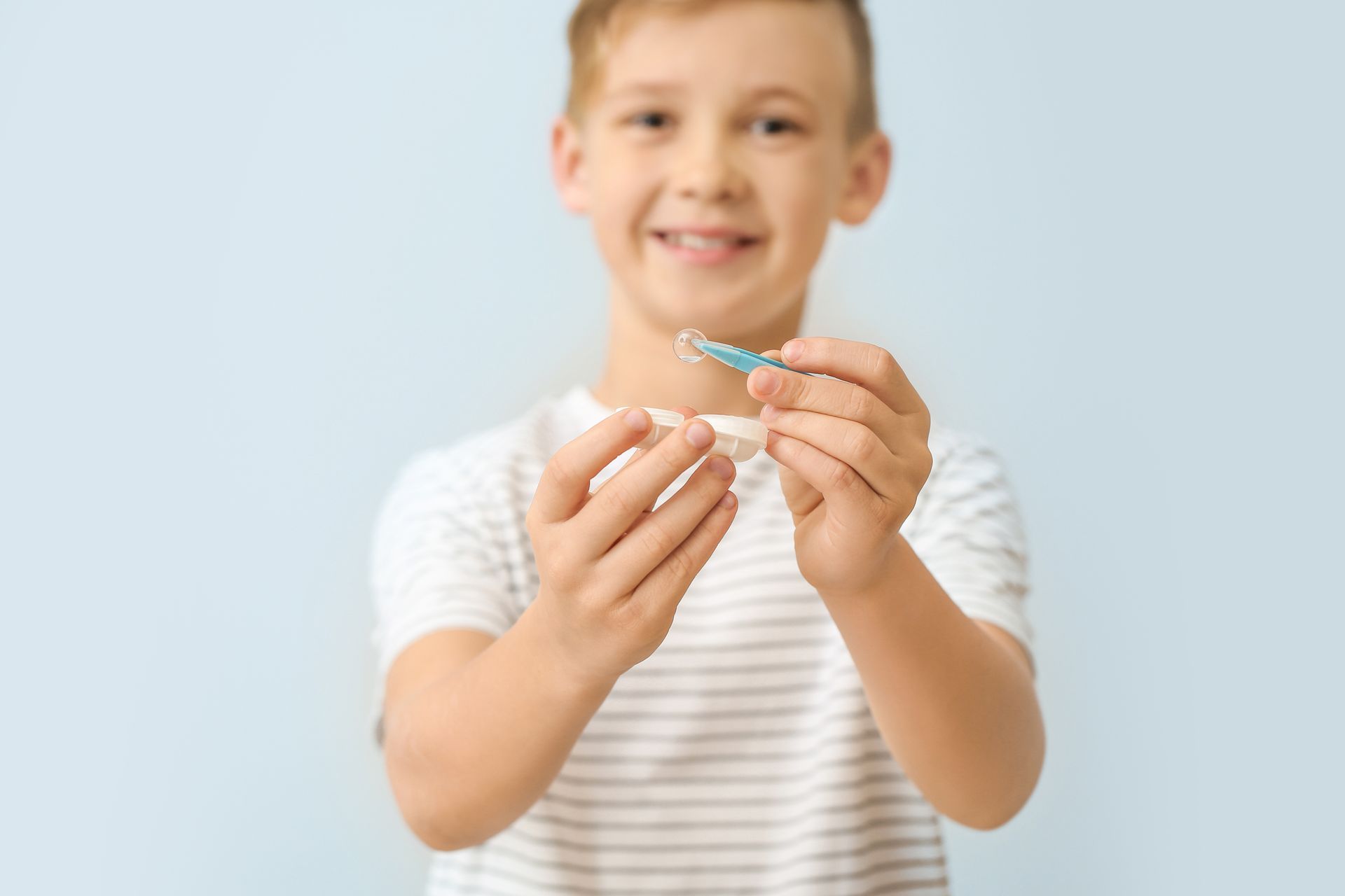 Smiling child holding a small blue object against a light blue background