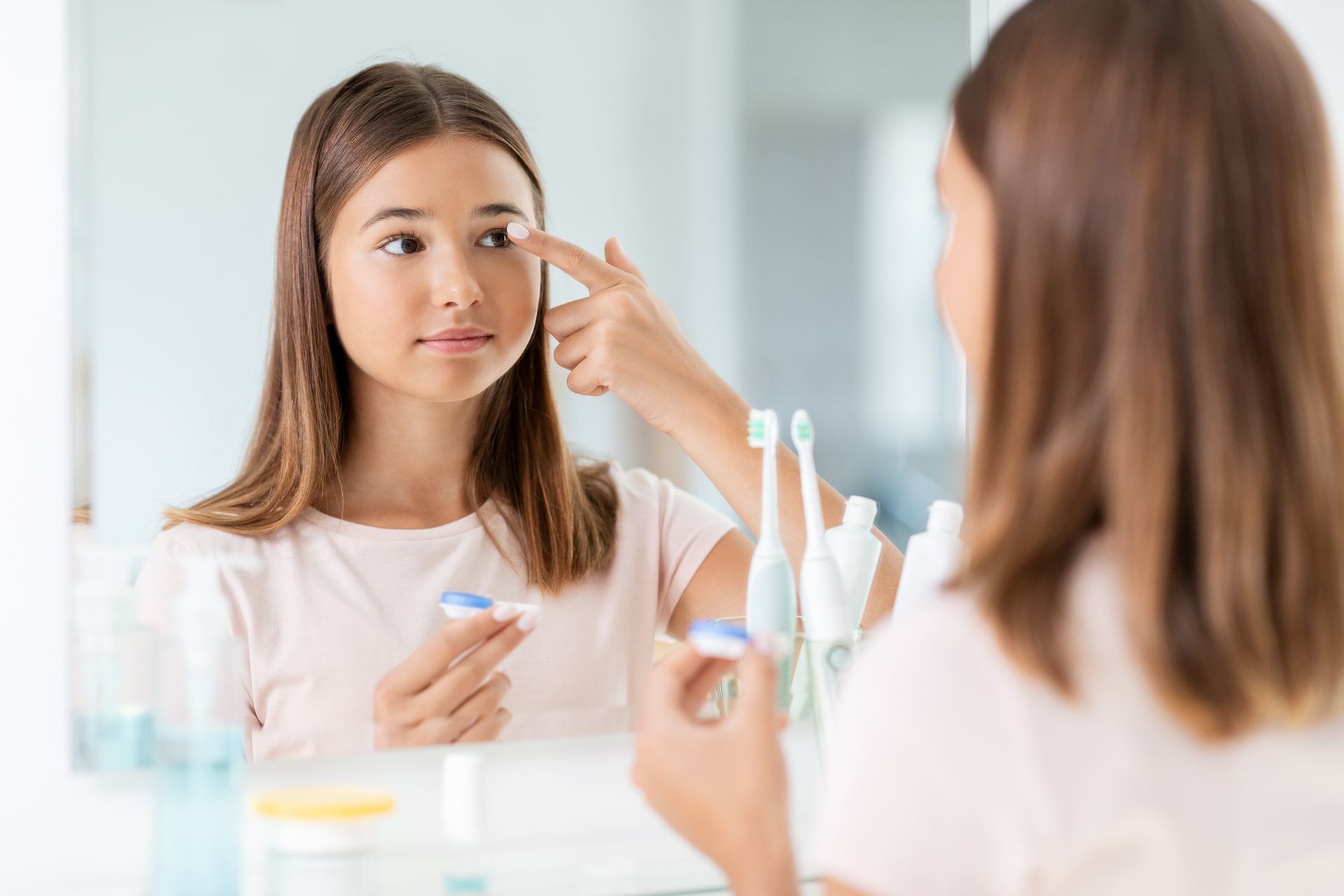 Woman applying eye makeup in front of a bathroom mirror, holding a cosmetic pencil.
