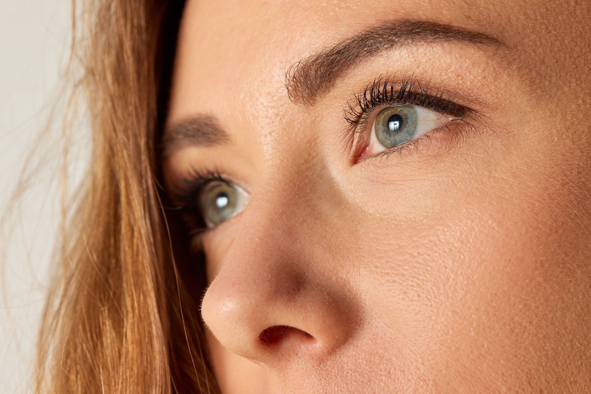 Close-up of a person’s blue eyes and nose, with brown hair against a light background