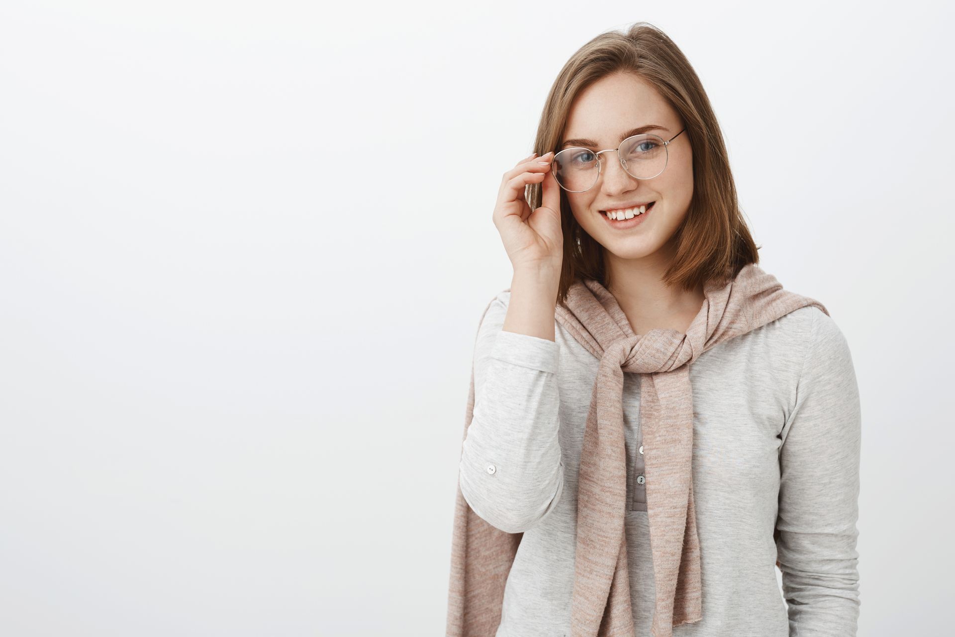 Smiling person in glasses and a scarf, adjusting them against a plain white background