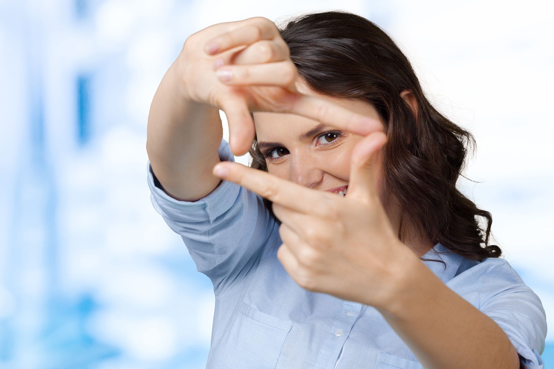 Person framing a shot with hands, looking through fingers, in a blue shirt against a blurred background
