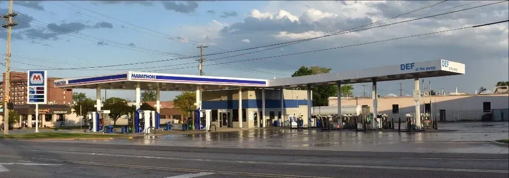 Gas station under a cloudy sky with wet pavement and a few cars in the lot