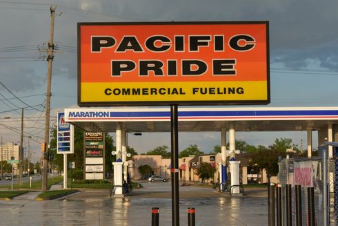 Pacific Pride commercial fueling station sign with pumps beneath, at a roadside lot at sunset