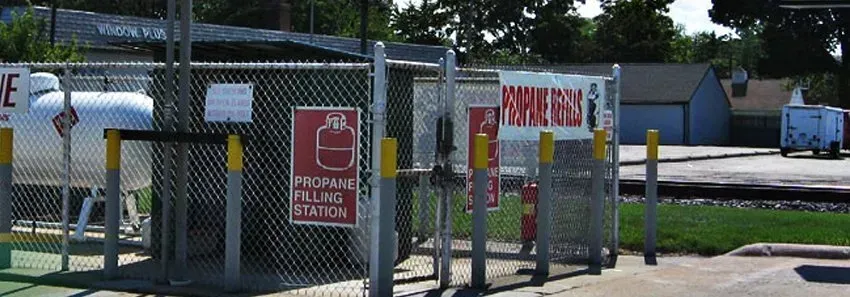 Chain-link fenced entrance with red warning signs and a gate beside a paved road