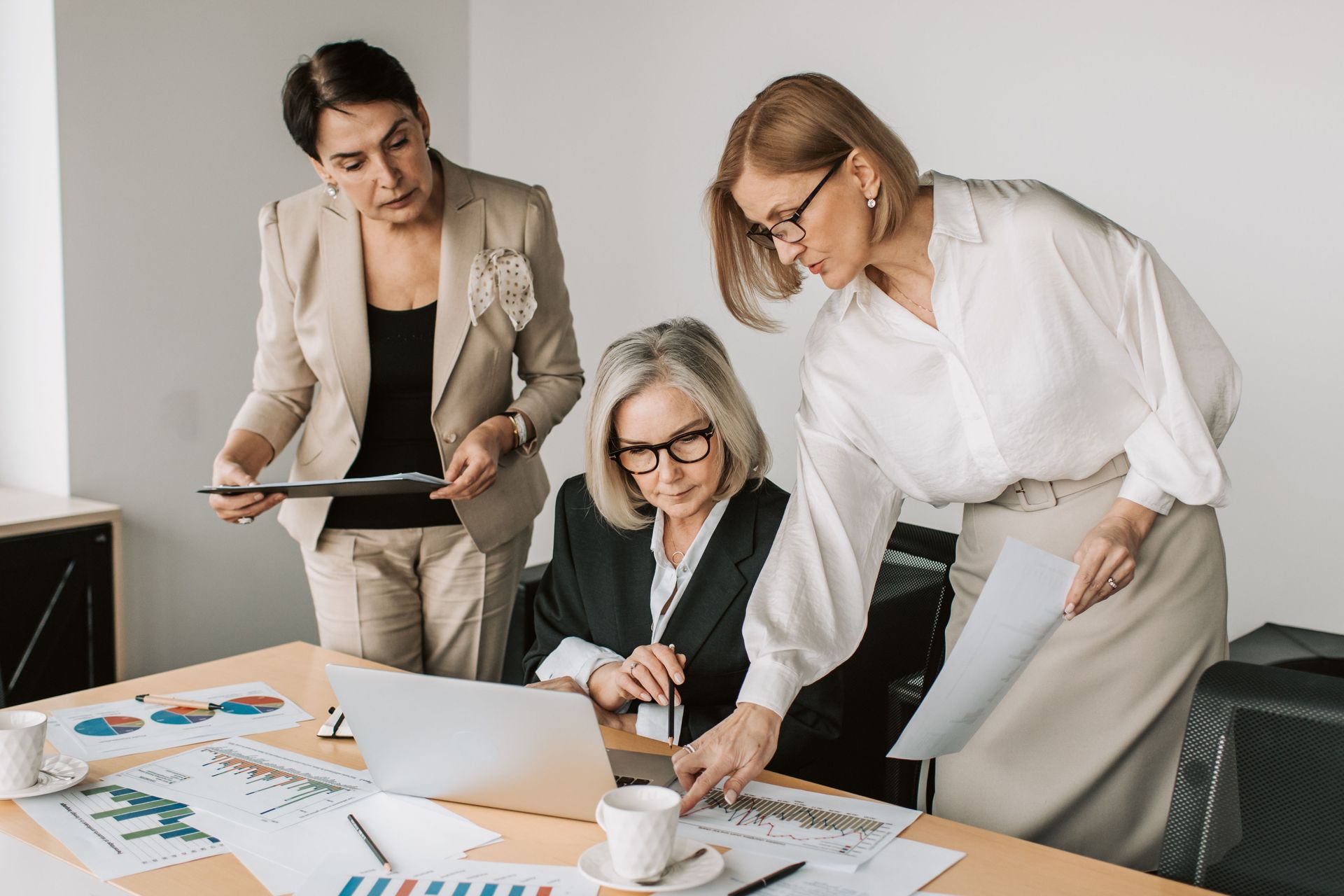 Three coworkers reviewing charts and a laptop during a business meeting in a bright office