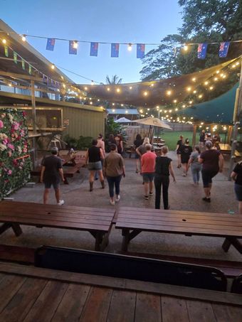 People dancing at an outdoor evening gathering with string lights and flags overhead.