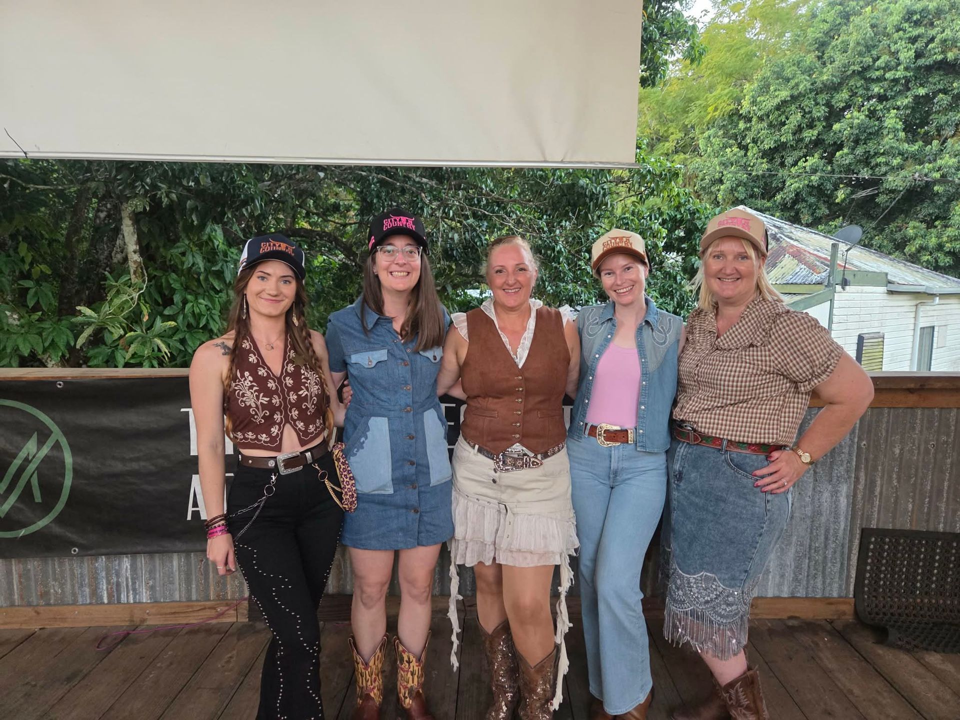 Five people posing together outdoors, smiling in front of a green garden backdrop.