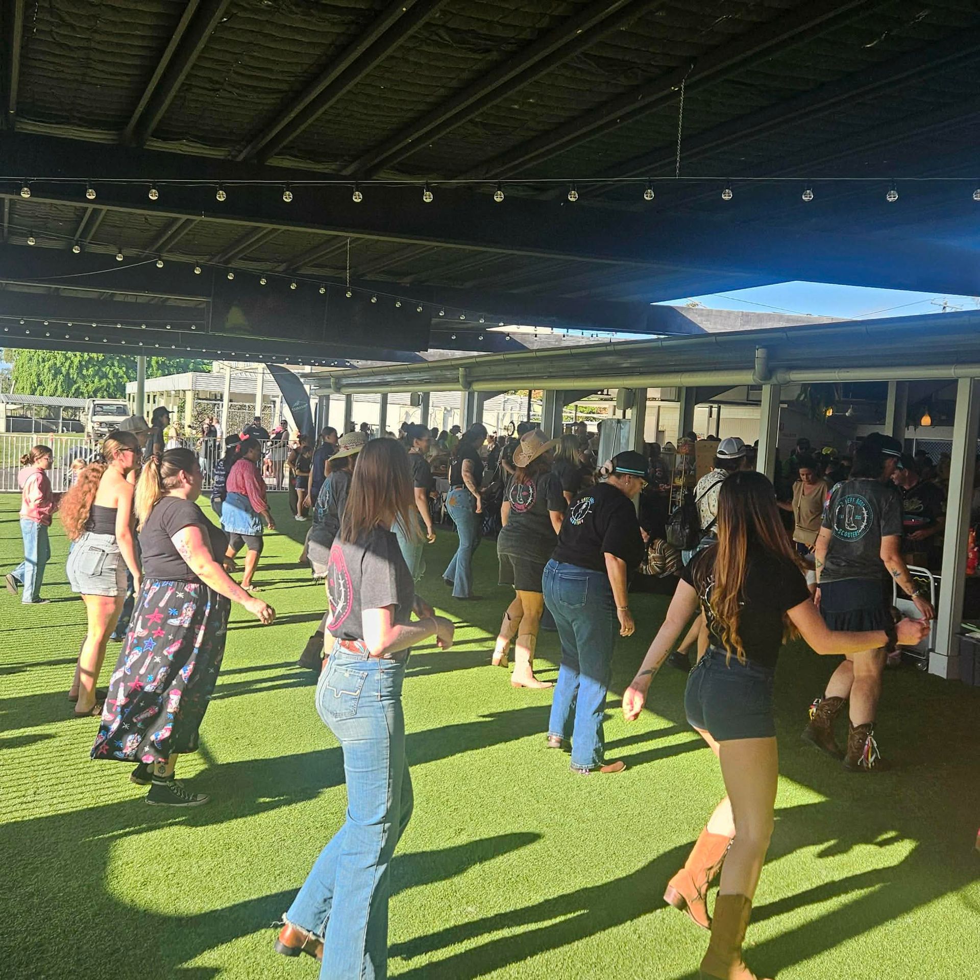 People exercising in a covered outdoor fitness class on green turf in bright sunlight