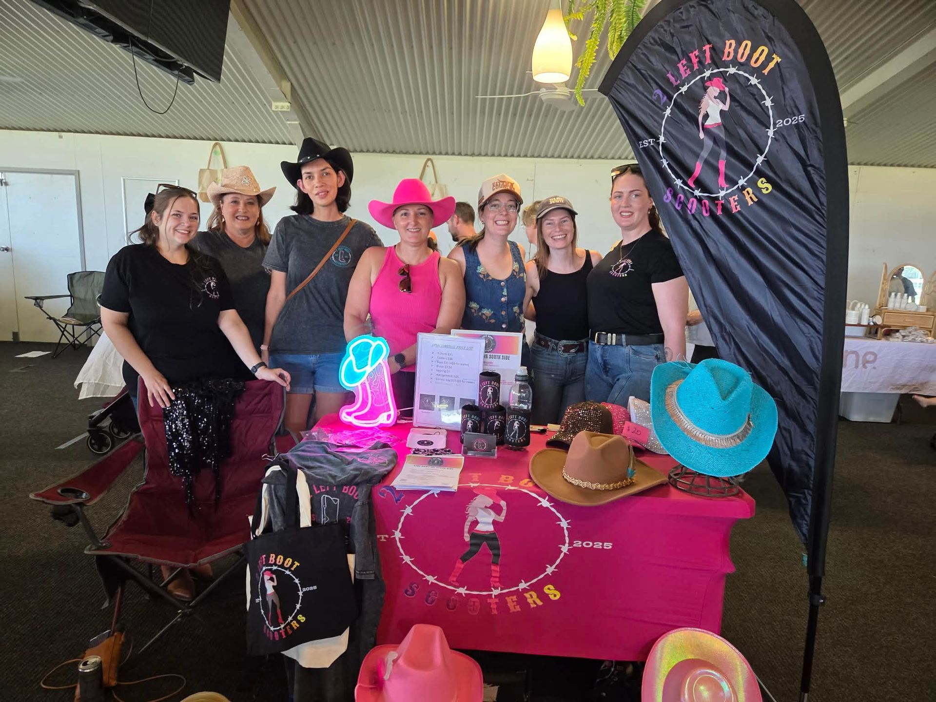 Group at a vendor booth with bright pink hats, signs, and Western-style decor under a tent
