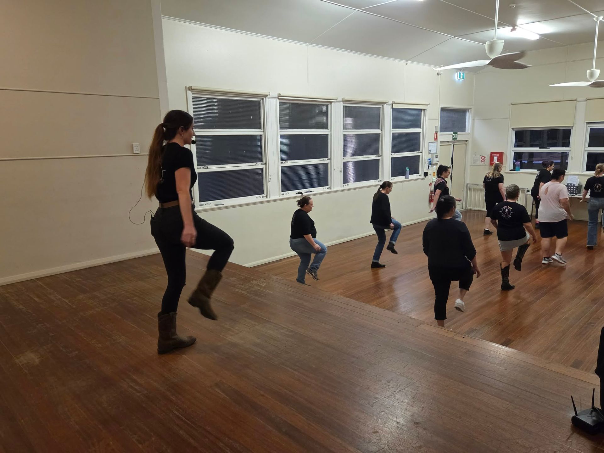 Adults exercising in a bright studio, stepping in sync on a wooden floor.