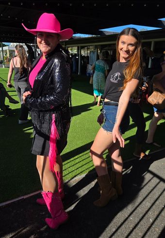 Two people dancing outdoors in bright cowboy hats and boots at a sunny event