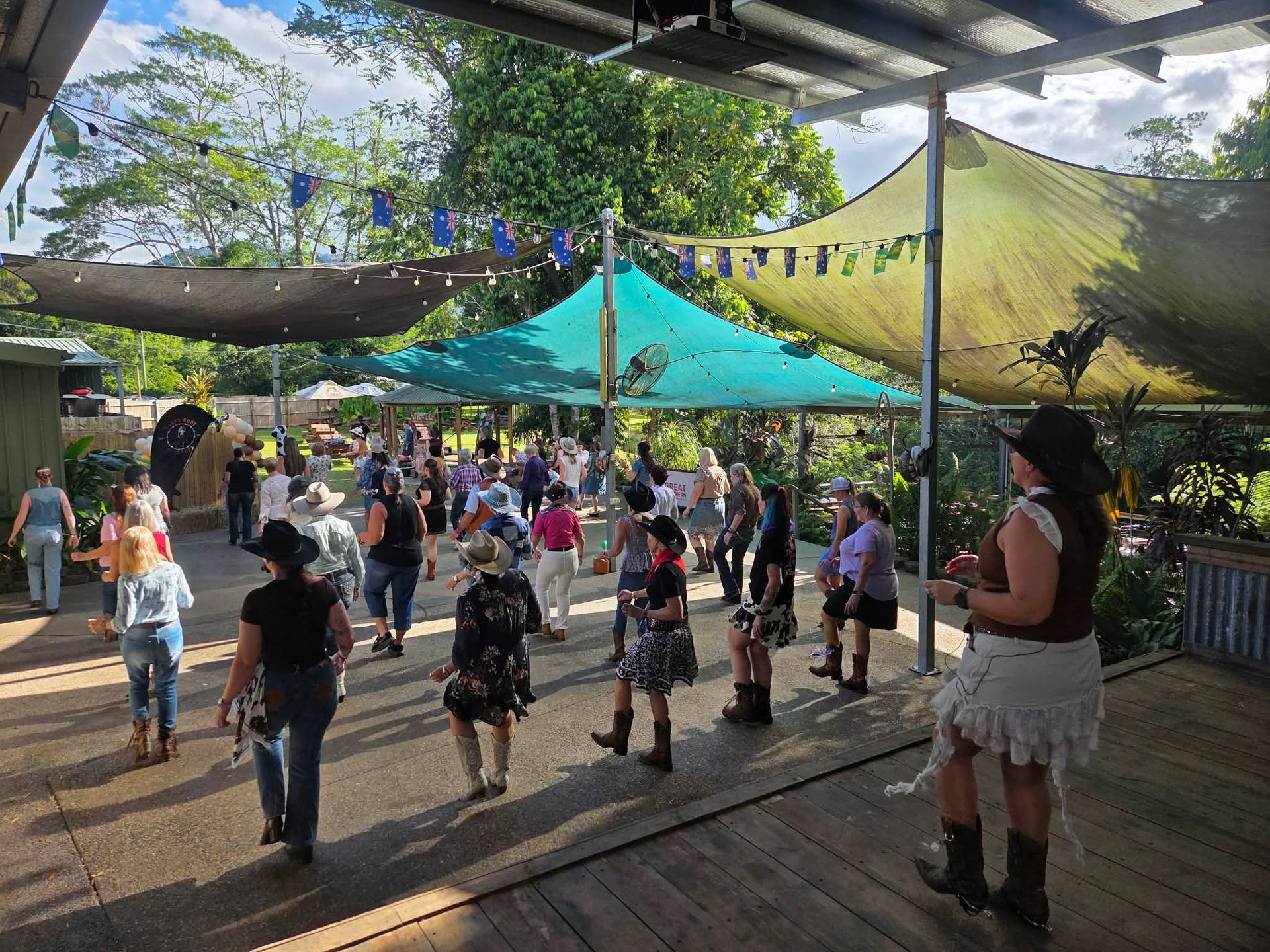People dancing under shade canopies at an outdoor gathering with colorful bunting.