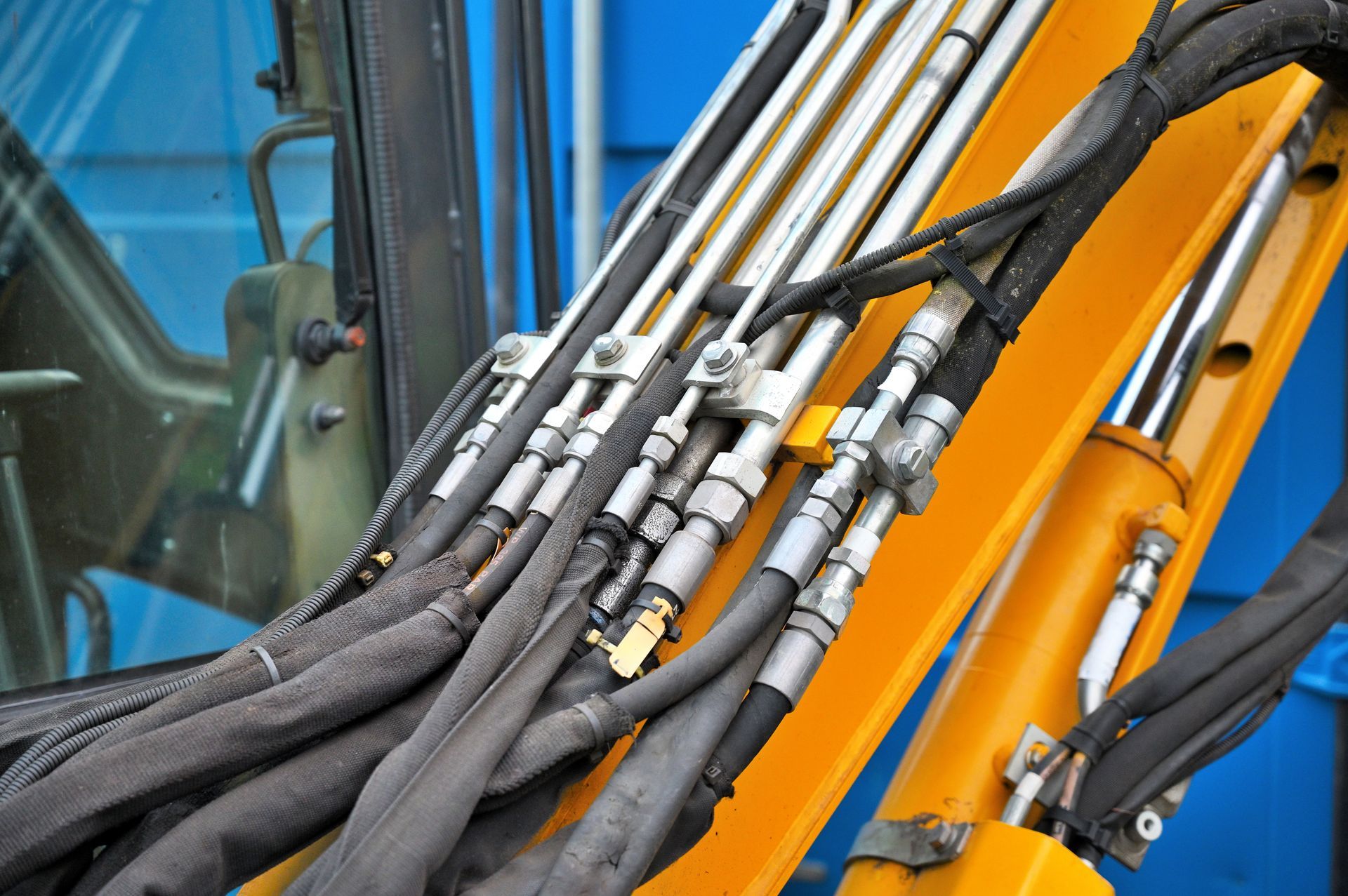 Hoses of modern hydraulic machine. Hydraulic hoses and metal connectors on a yellow excavator arm against a blue machine cab
