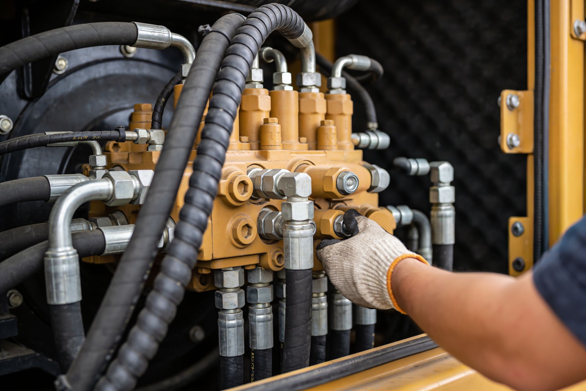 Close-up of a gloved hand adjusting hydraulic valve connections on industrial machinery.