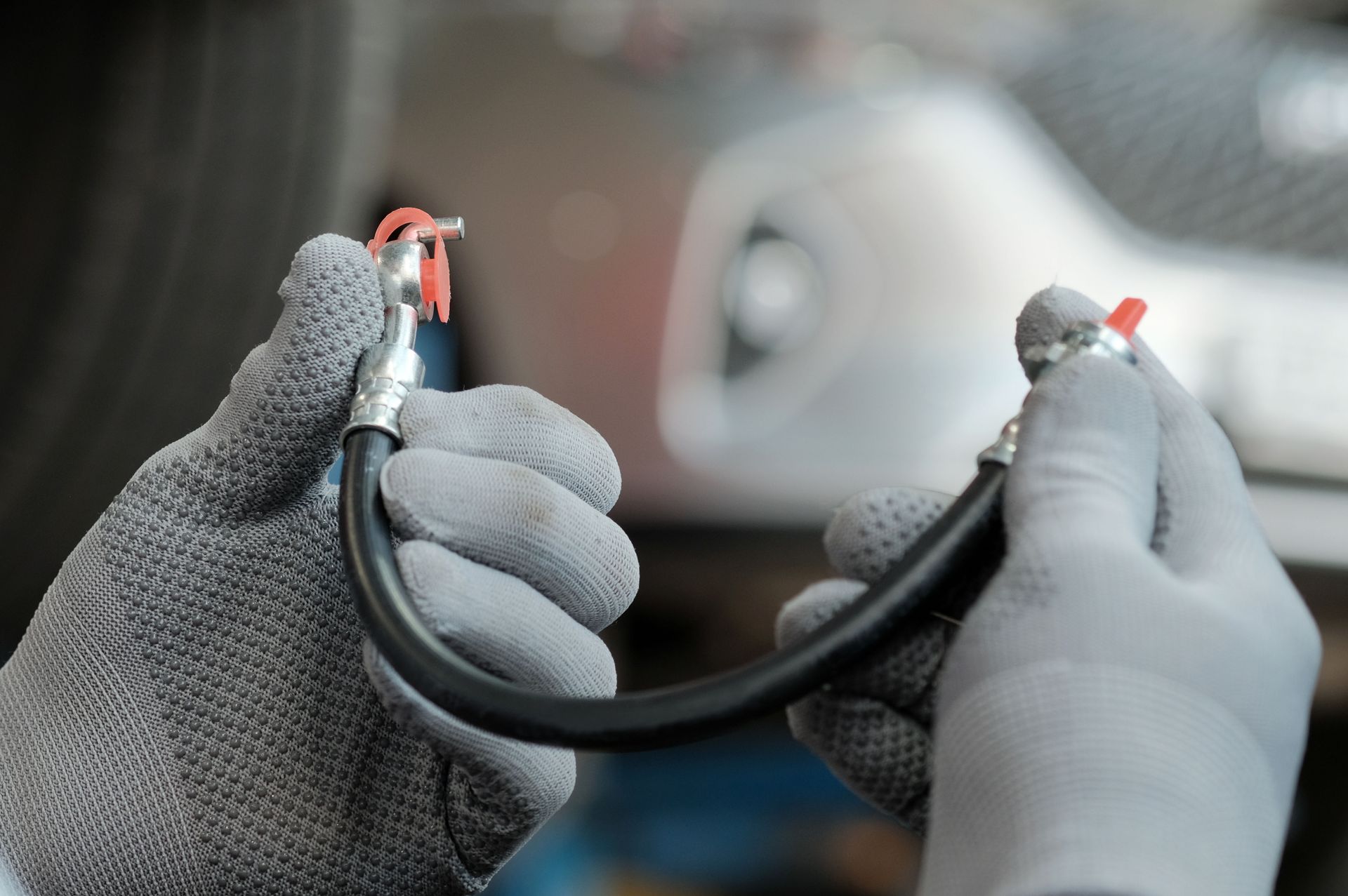 Hands in gray gloves holding a black cable with exposed red connectors, close-up in a workshop.