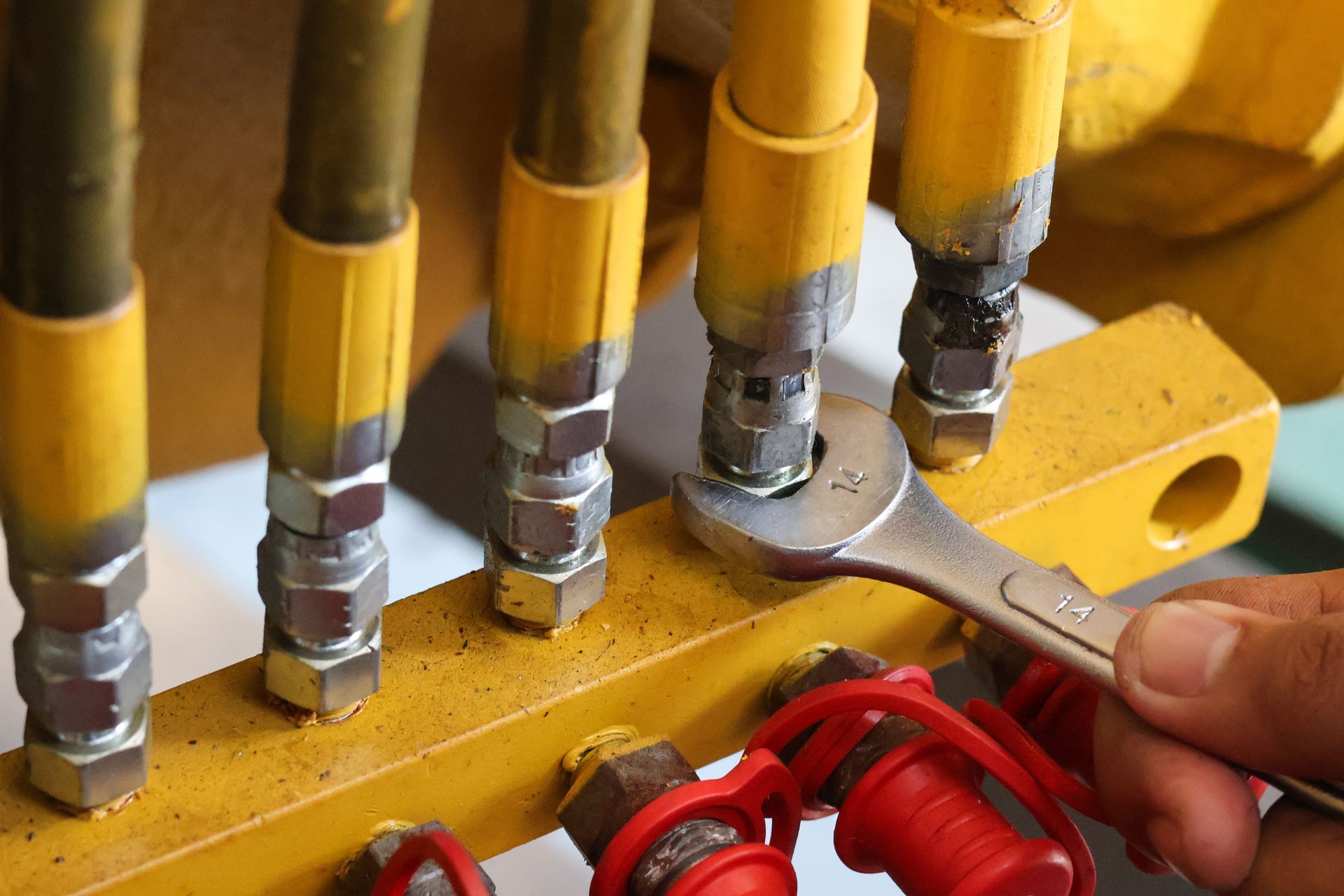 Close-up of hands using a wrench on yellow hydraulic hoses and fittings in a workshop.