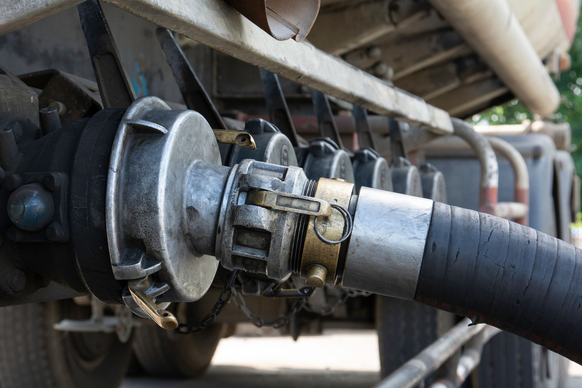 Close-up of a tanker truck's hose couplings, with silver and brass connectors, connected to a black hose.