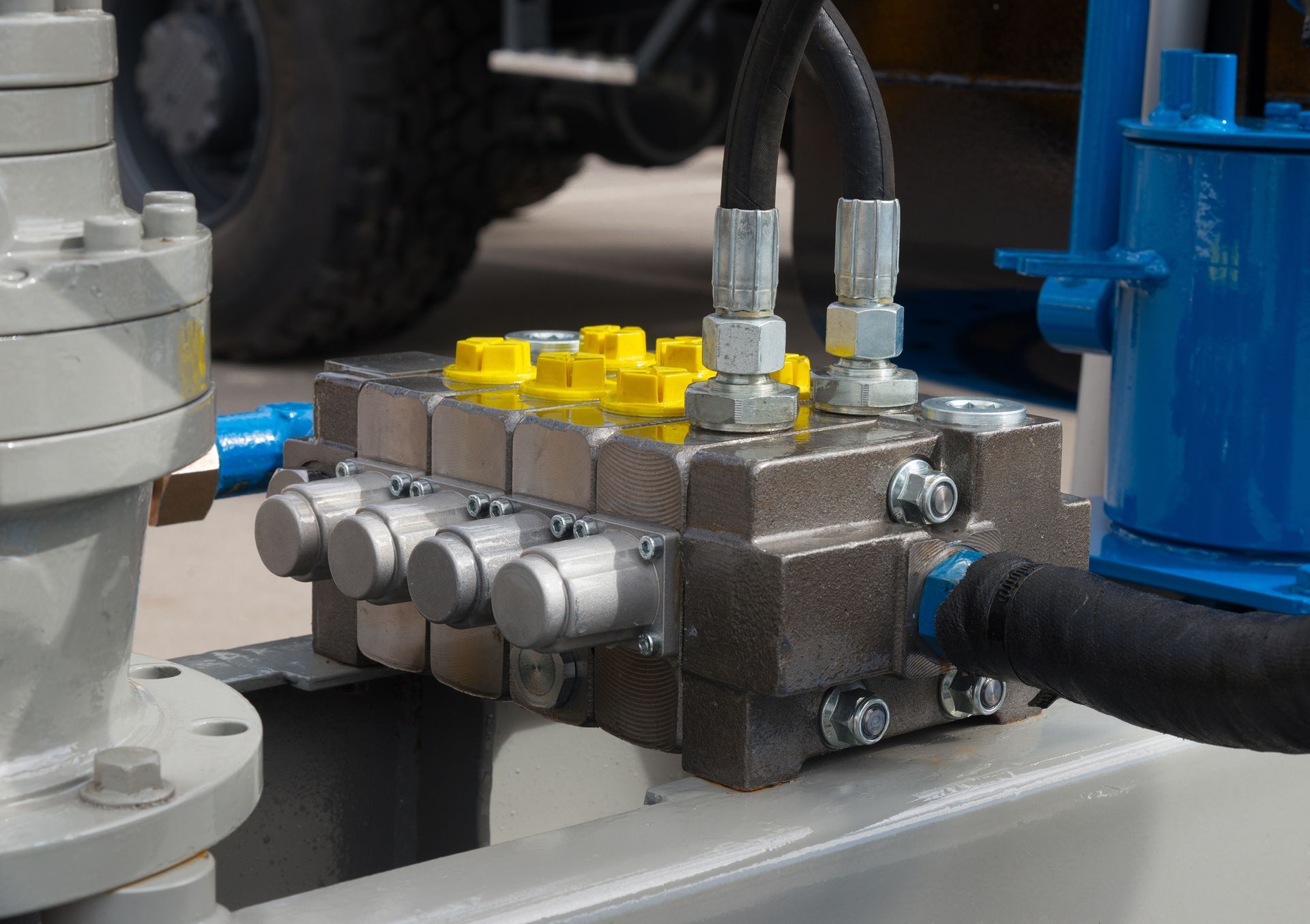 Hydraulic control valve with black hoses, yellow caps, and silver levers, mounted on industrial machinery.