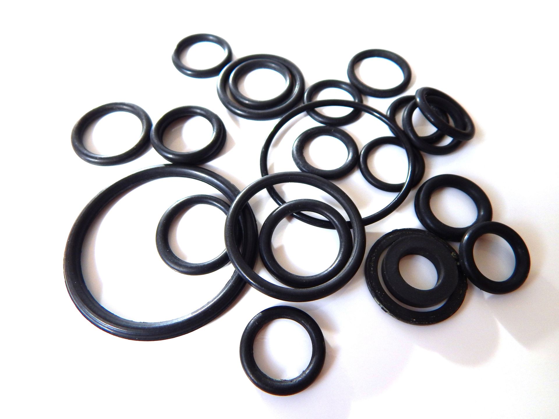 Scattered collection of black rubber O-rings of various sizes on a white surface, presumably for sealing purposes.