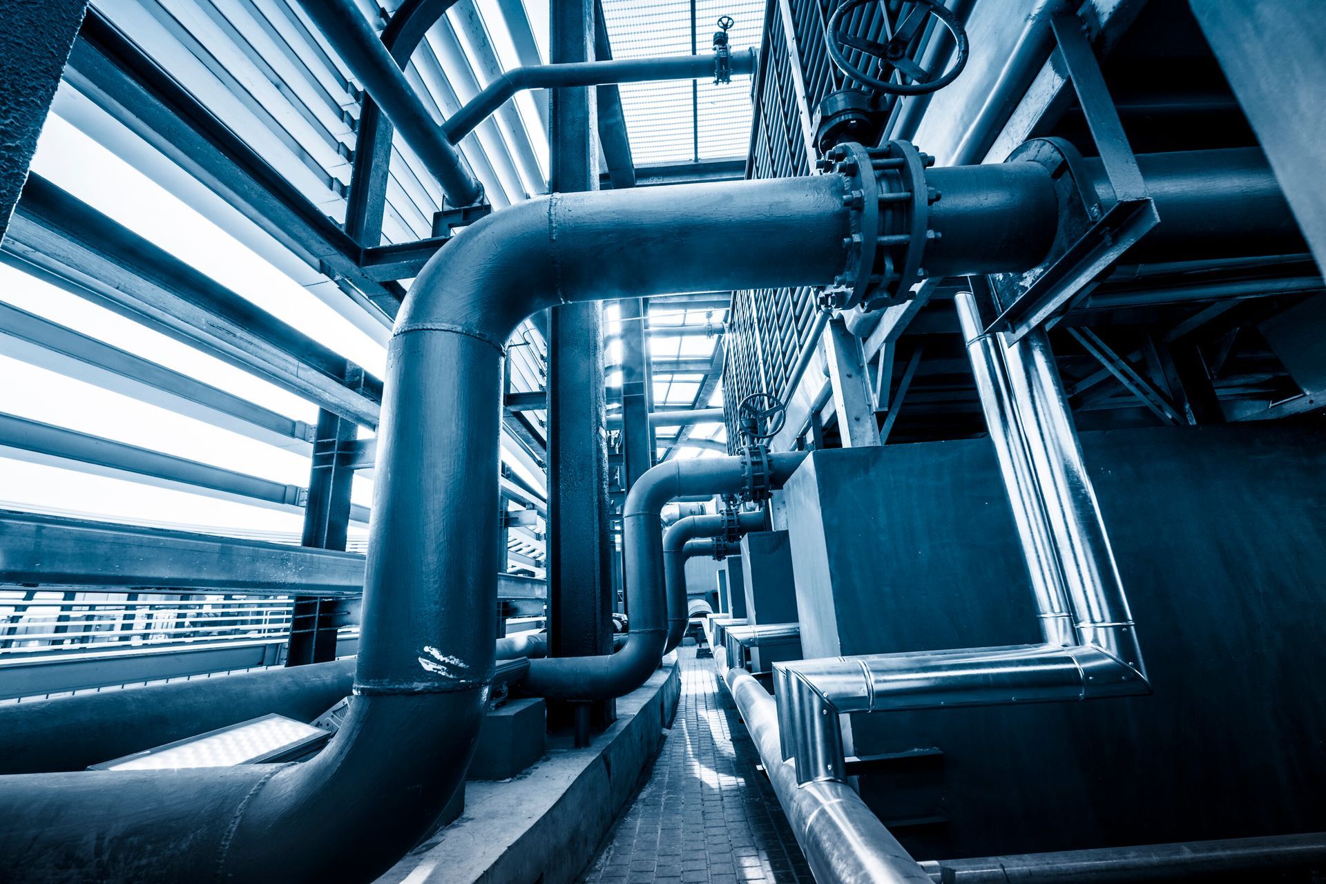 Blue-toned photo of industrial pipes and machinery in a large, metallic setting.