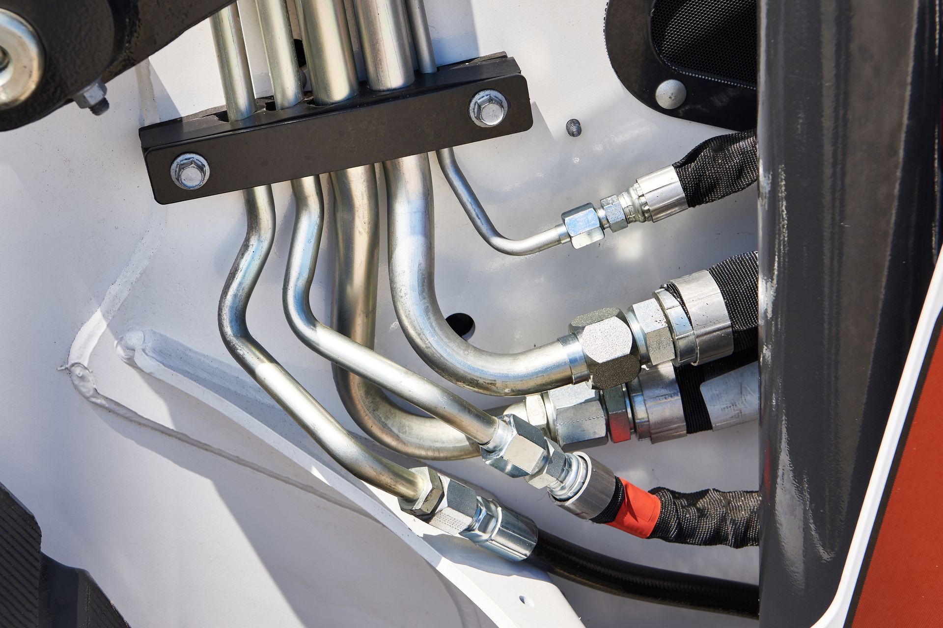 Close-up of hydraulic lines on a piece of heavy machinery, including curved metal tubes, black hoses, and connected fittings.