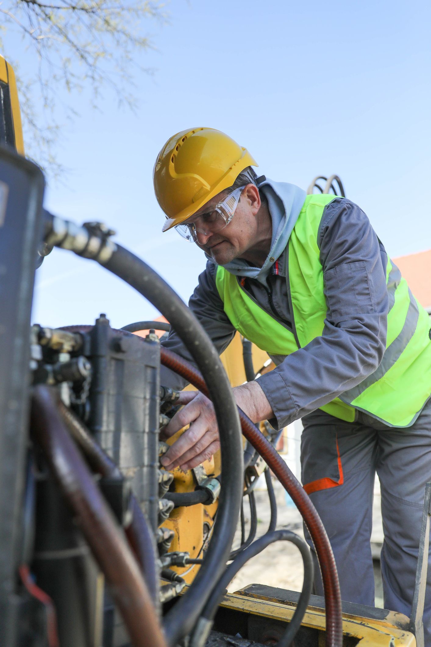 A male technician wearing a work uniform repairs hydraulic components on construction machinery