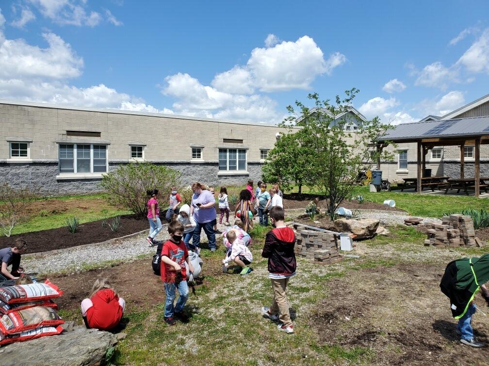 A group of children are working in a garden in front of a building.