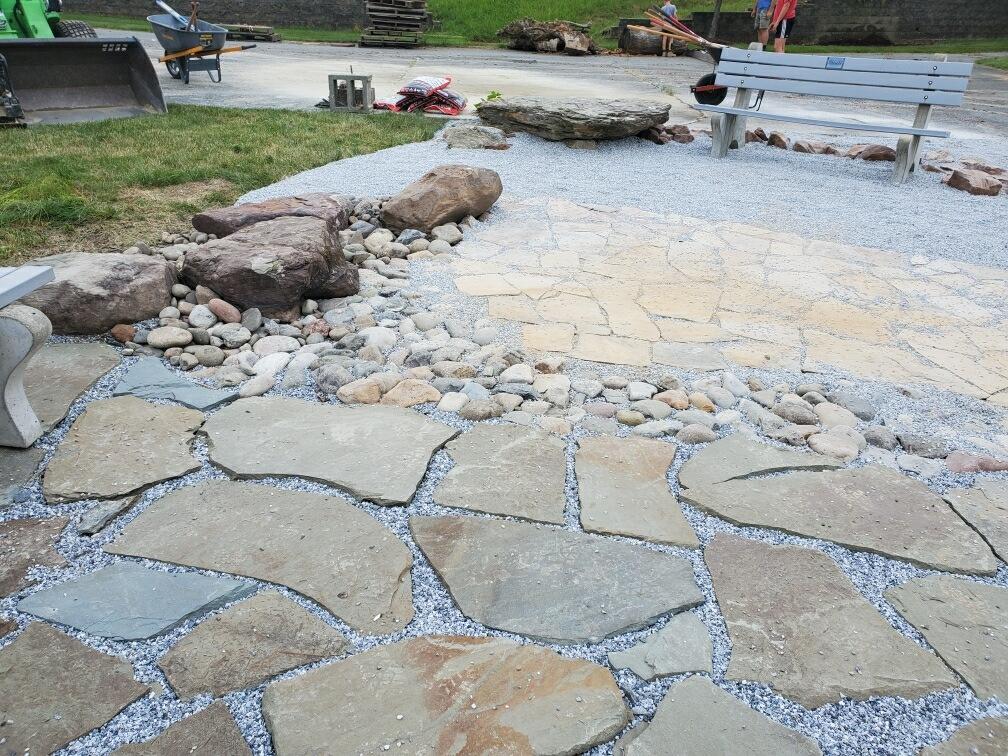 A patio with rocks and gravel and a bench in the background