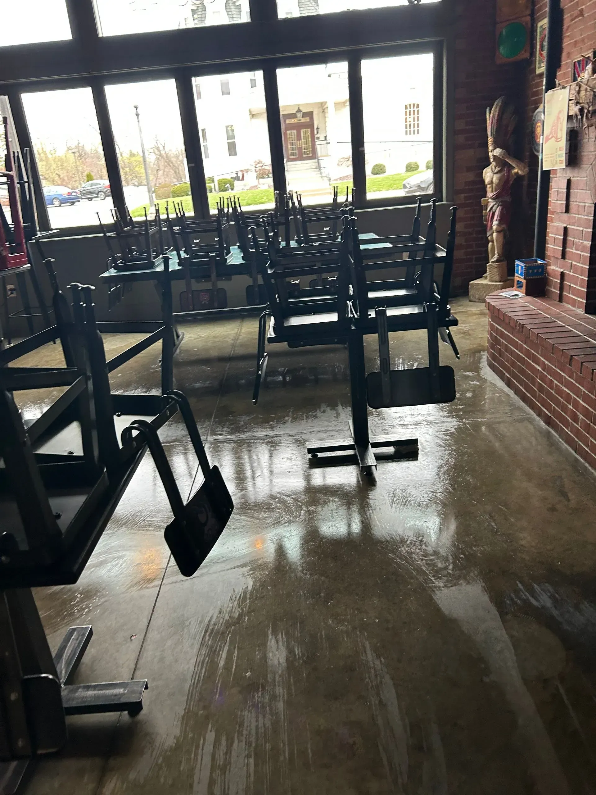 Empty restaurant with chairs stacked on tables; wet, reflective floor. Large windows.
