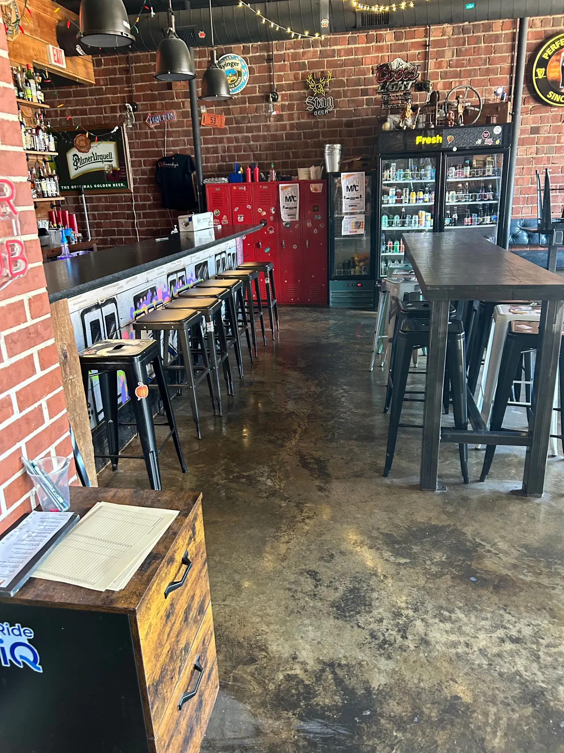 Interior of a bar with a brick wall, bar stools, and tables. A menu sits on a wooden stand.