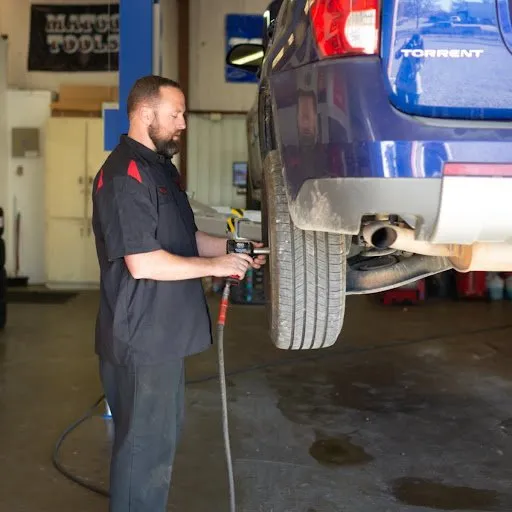 Mechanic removing a car tire with a pneumatic wrench in a garage.
