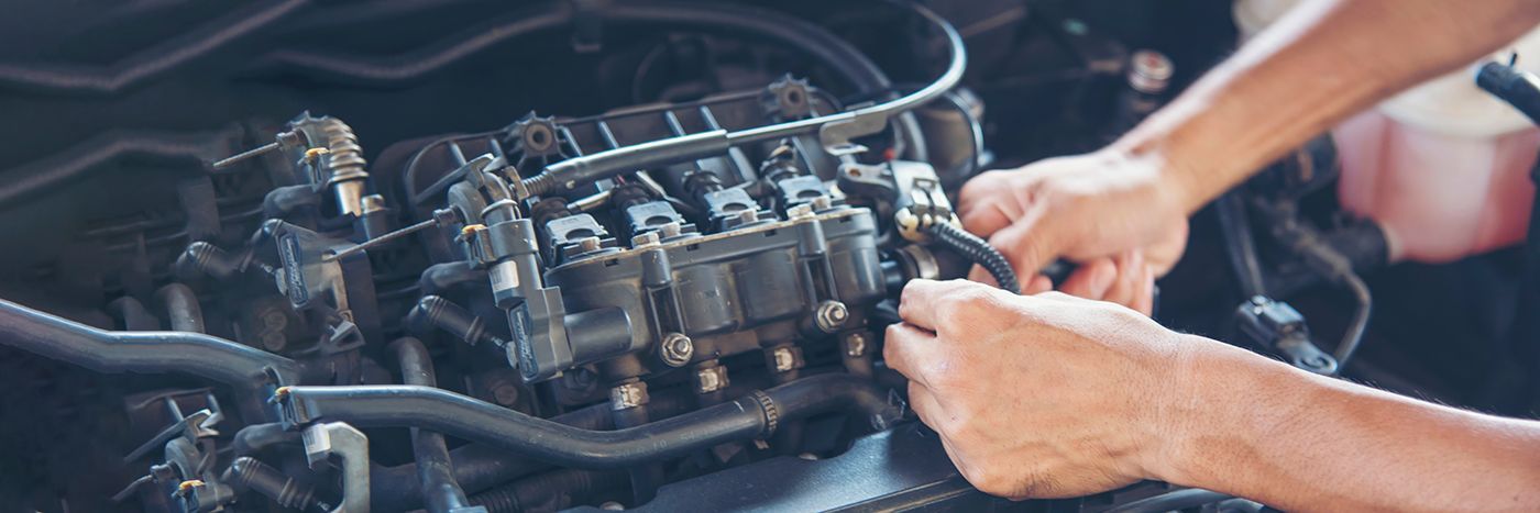 Mechanic tightening bolts on a car engine with a wrench in a garage.