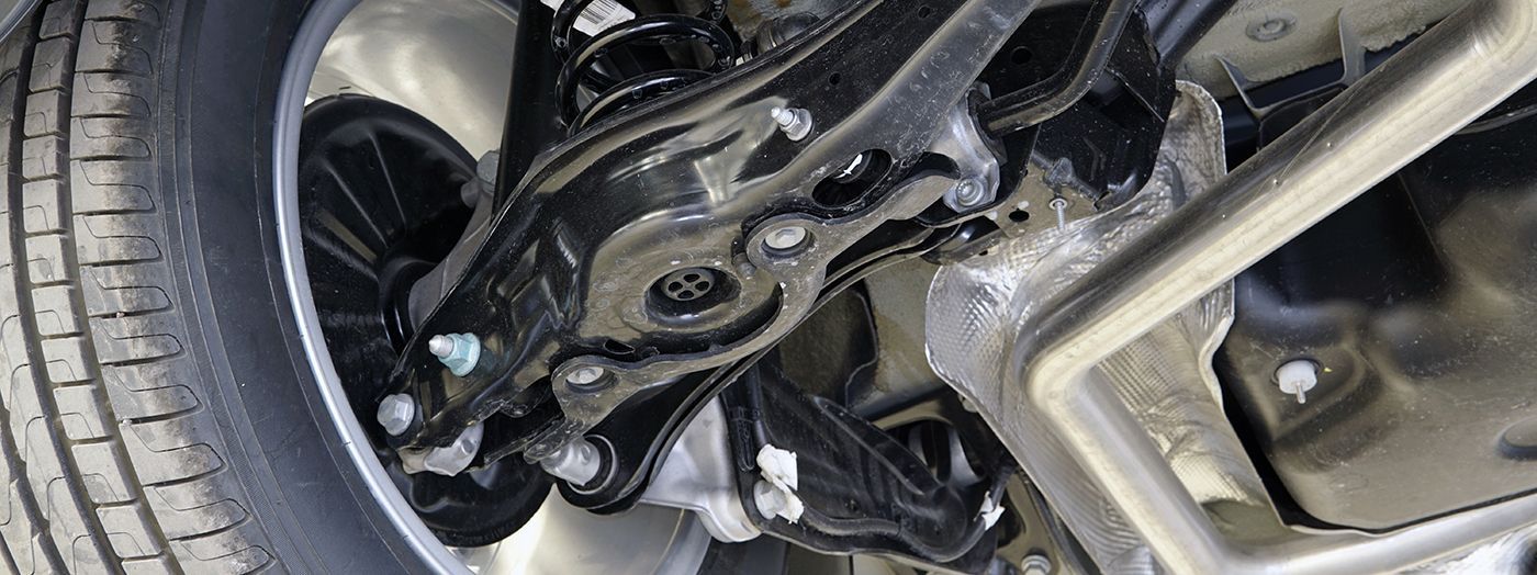 Undercarriage of a black vehicle, showing suspension components, tire, and wheel.