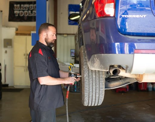 Mechanic uses power tool on lifted blue car tire in a garage.