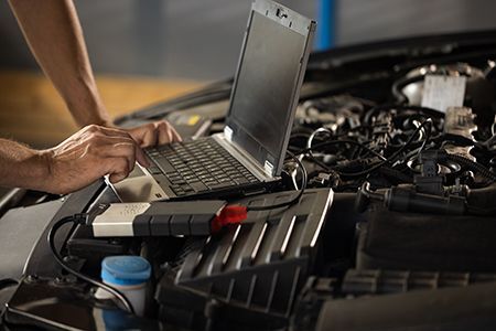 Mechanic using a laptop connected to a car engine for diagnostics.