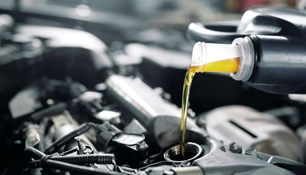 Pouring motor oil into a car engine; yellow liquid, blurry background.