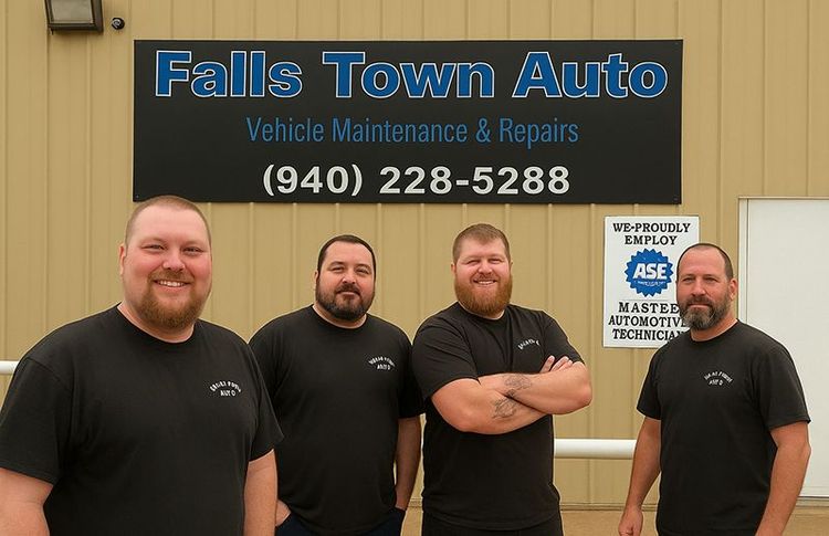 Four men in black shirts standing in front of a Falls Town Auto sign, smiling.