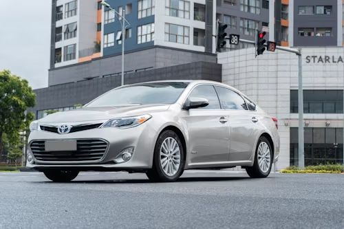 Silver Toyota Avalon sedan parked on a wet street in front of a modern building.