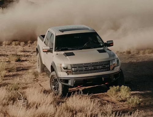 Ford Raptor truck driving through dusty terrain.