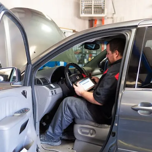 A man is sitting in the driver 's seat of a car using a tablet.
