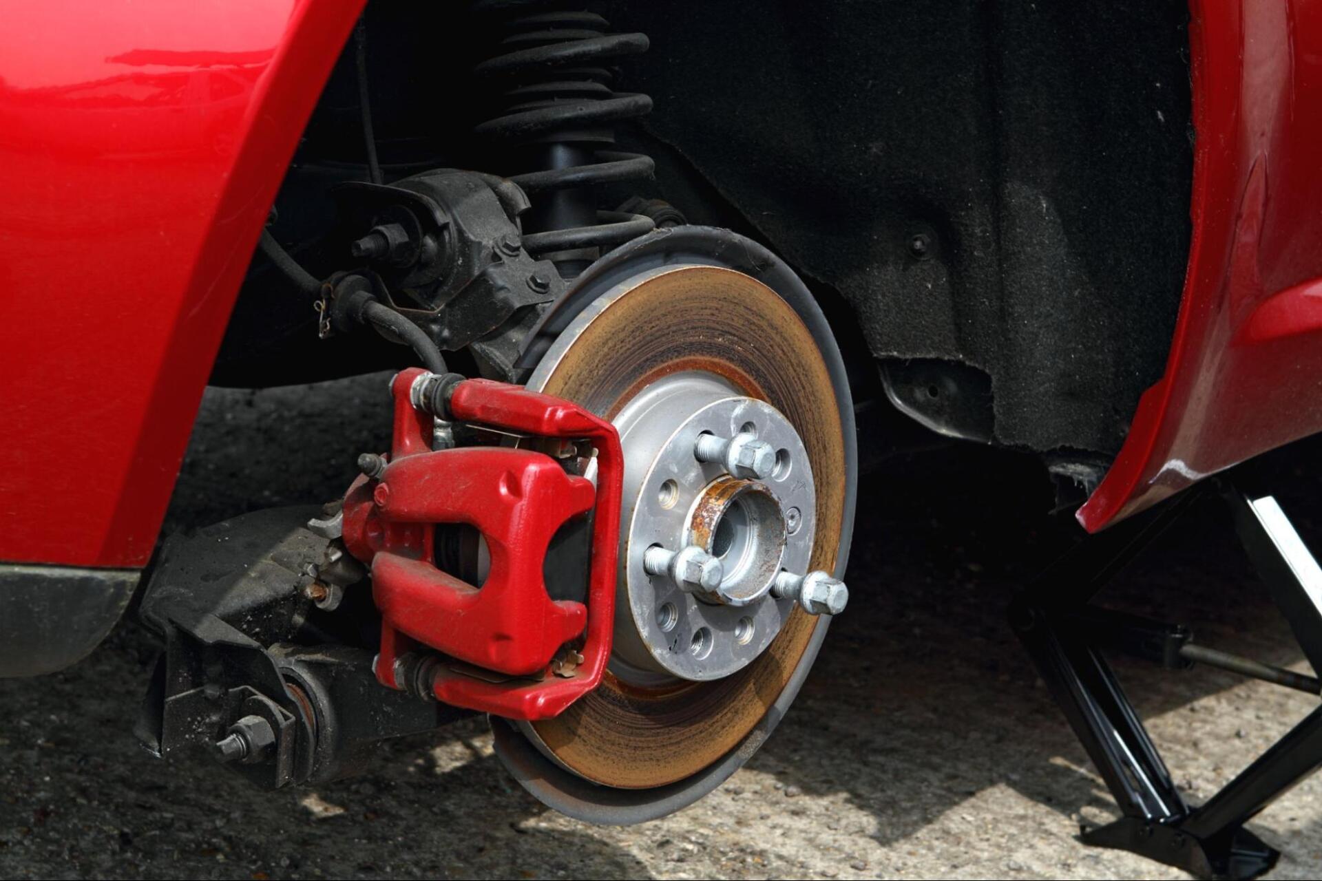 A red car with a red brake caliper is sitting on a jack.