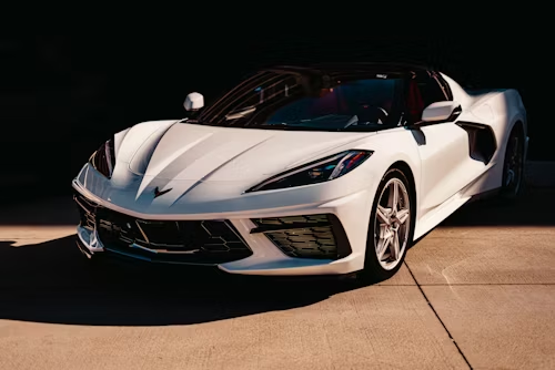 White sports car parked in front of a dark background, with the sunlight illuminating its features.