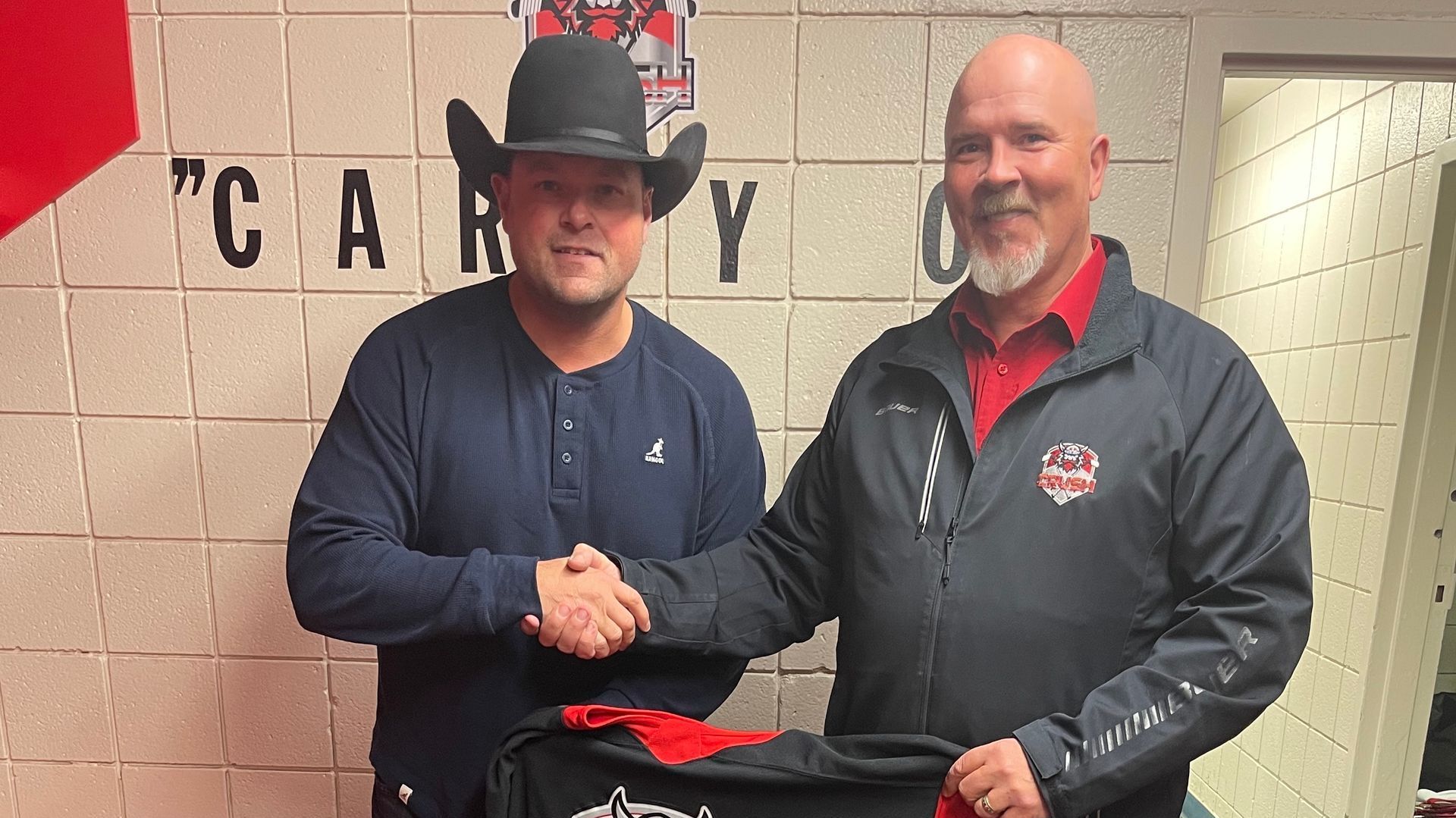 Colin Grindle and country singer/songwriter Gord Bamford shake hands holding a Camrose Crush jersey